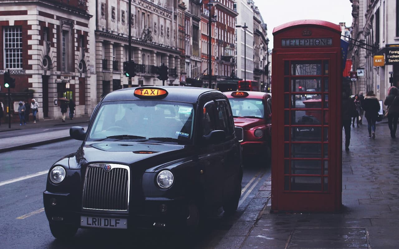 A London black taxi parked on a city street beside a red telephone box
