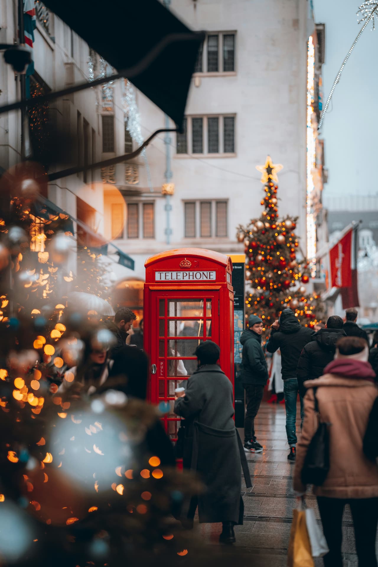 A red telephone box beside a lit Christmas tree in London